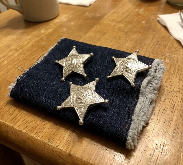 Reference photo of three sheriff badges pinned to a denim swatch